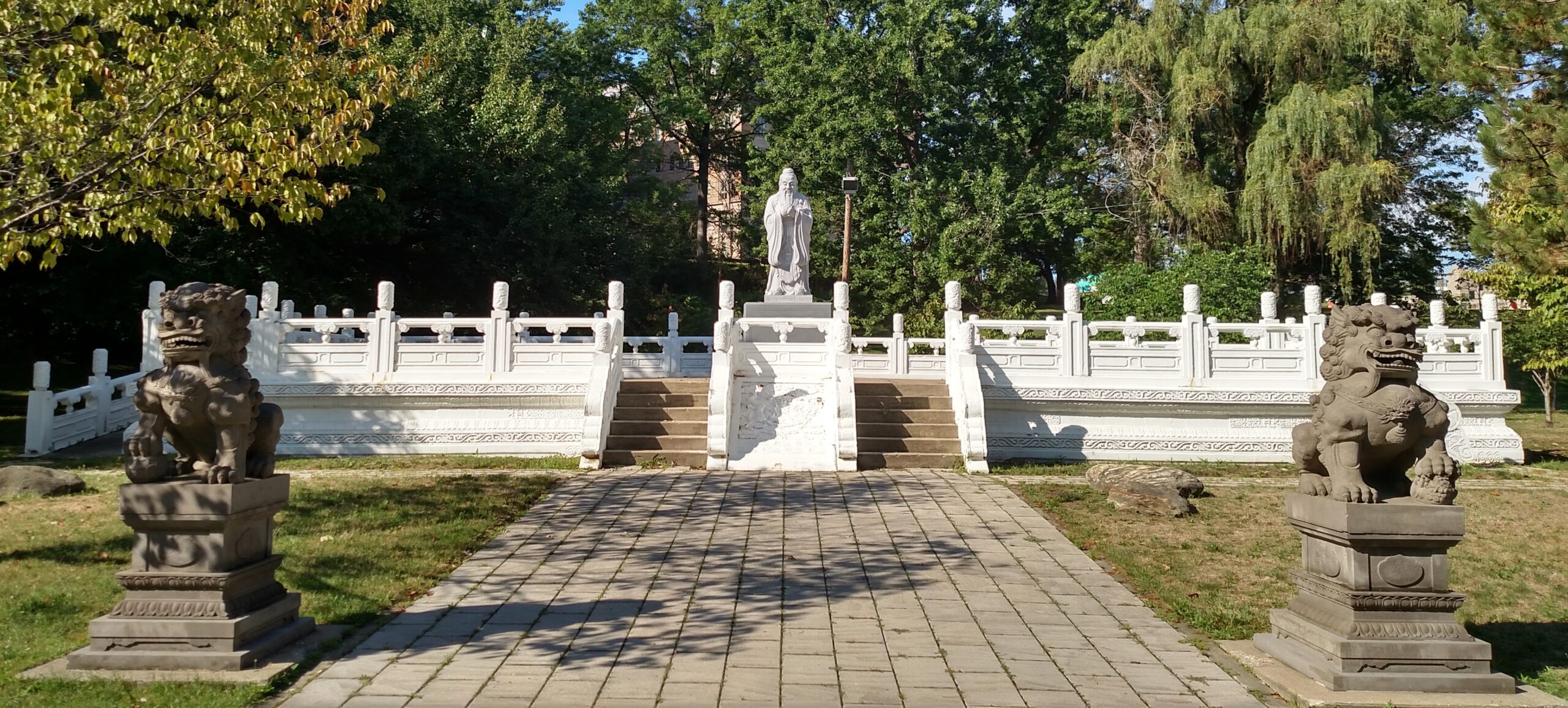 The traditional Imperial Chinese architecture of the Chinese Cultural Garden, including white marble railings and stone pathways, was designed to reflect harmony with nature. The entrance is flanked by two intricately carved Chinese dragons symbolizing strength and wisdom.